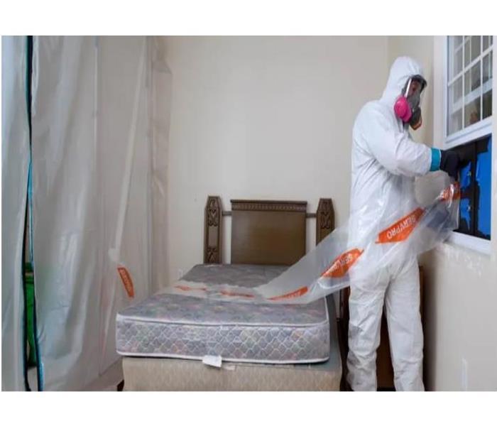 man in PPE in a bedroom with bed mattress 