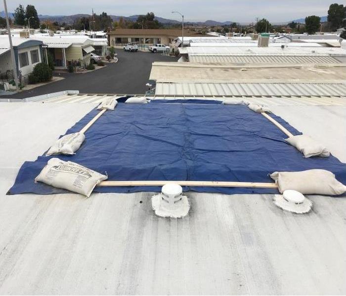 mobile home white flat roof, blue square tarp cover held by sand bags on each corner