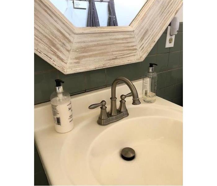 white bathroom sink with mirror above, clear bottle of hand soap and hand lotion on the sink.