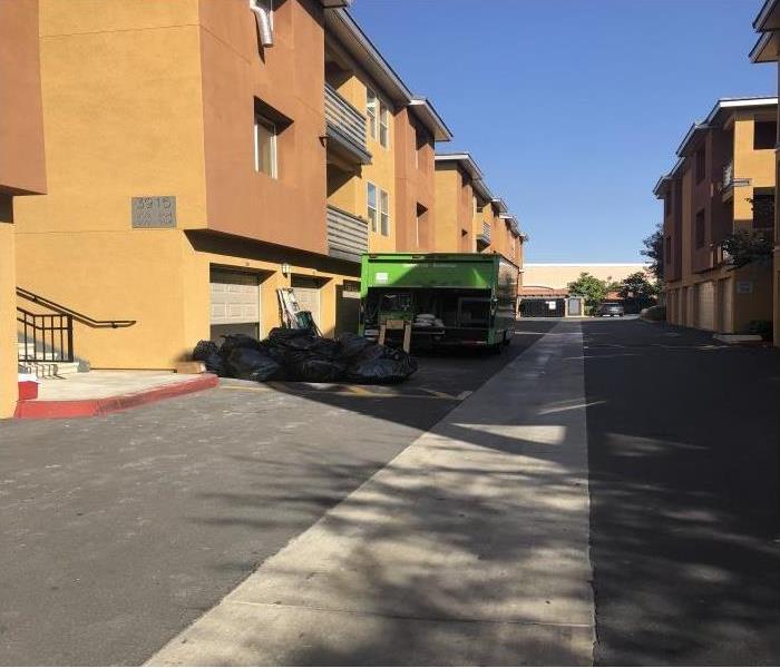 3 level orange apartment complex with a green SERVPRO truck in front of a garage with black trash bags behind truck.